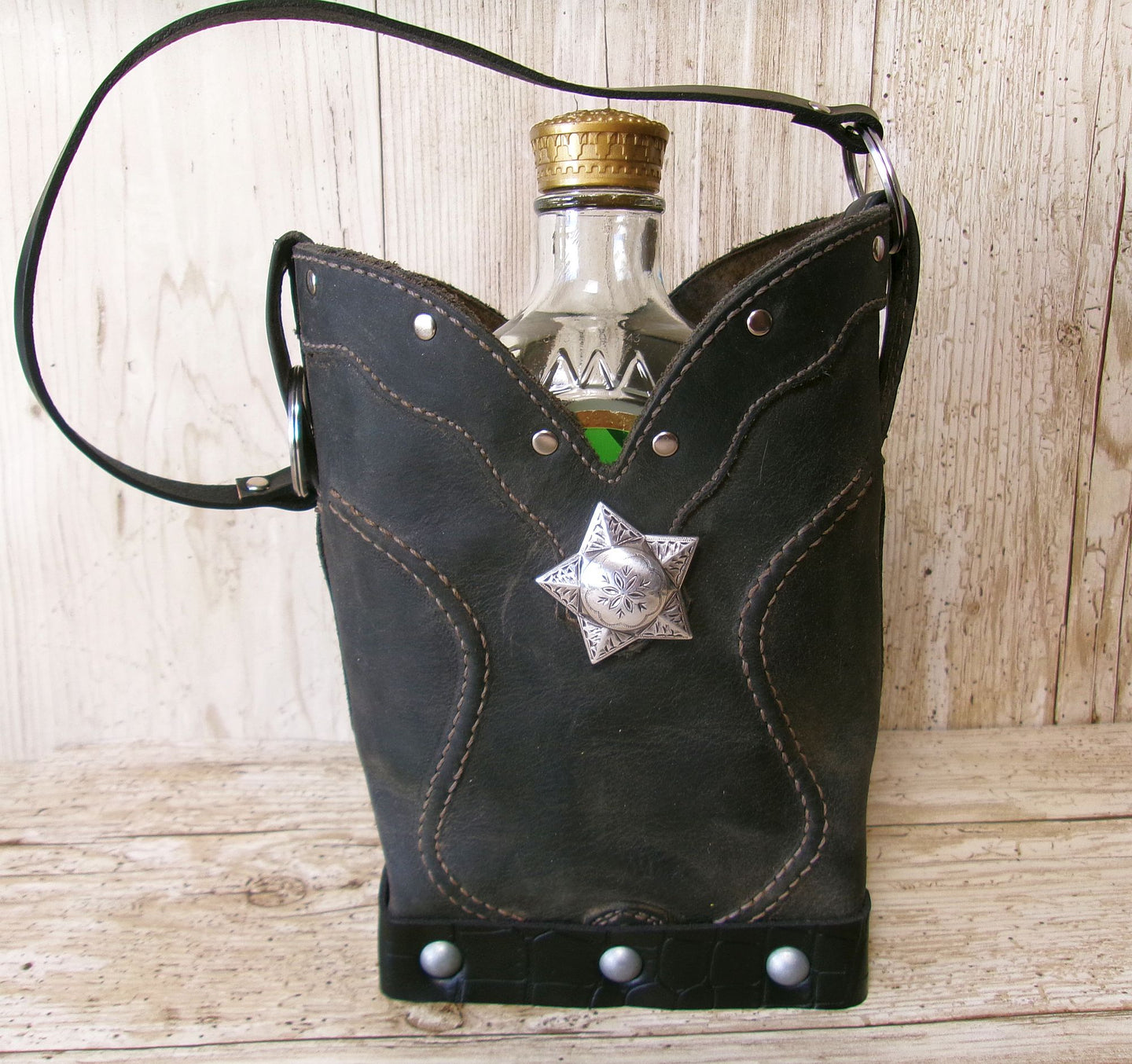 Black leather flask holder with star accent containing a bottle on a wooden surface